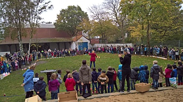 Auf dem Bild ist ein großer Singkreis mit allen Menschen der Schule zu sehen. 