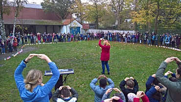 Auf dem Bild sieht man, wie alle Menschen der Schule den Tanz zu einem Lied tanzen.
